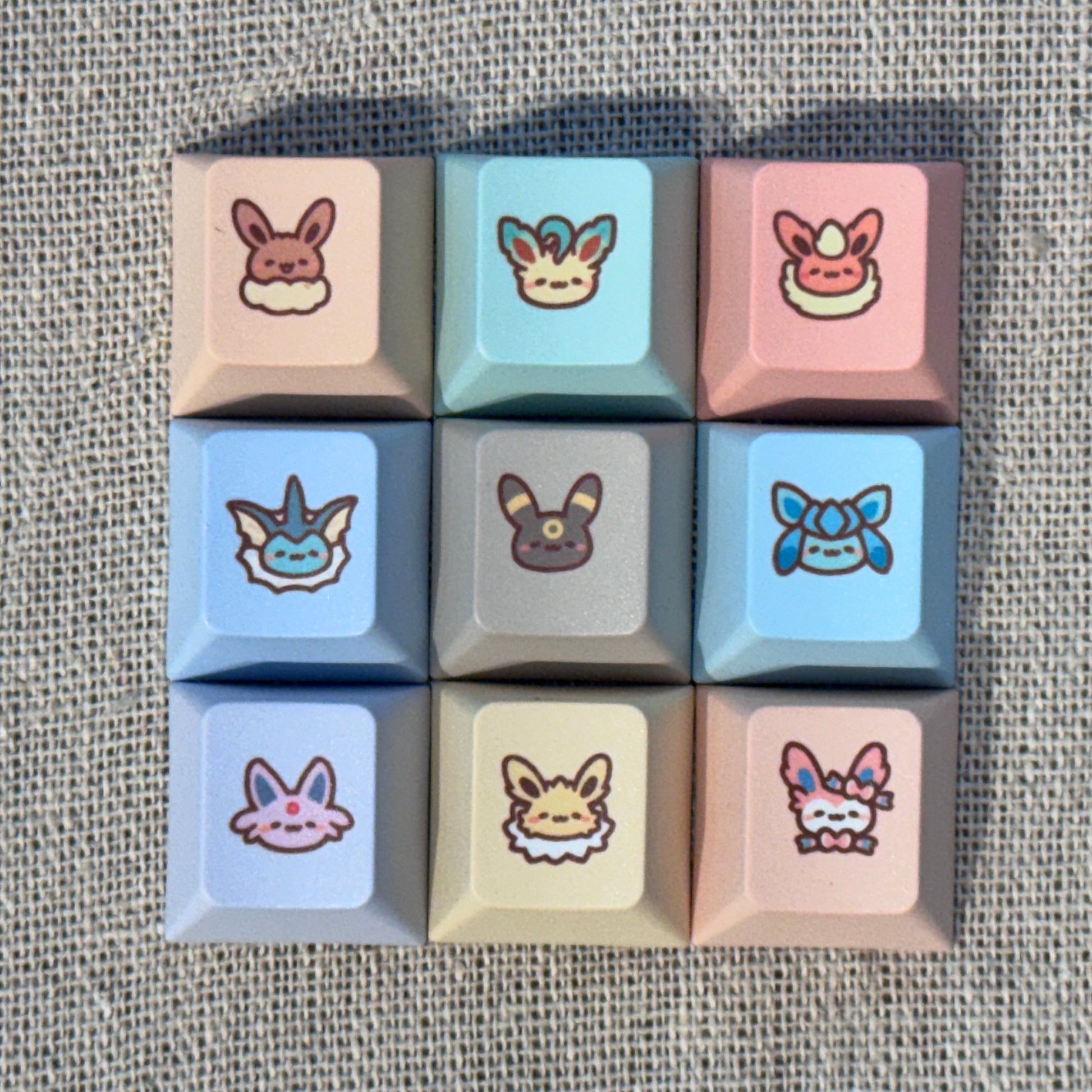 Nine pastel Pokémon Eeveelution keycaps featuring Eevee, Vaporeon, Jolteon, Flareon, Espeon, Umbreon, Leafeon, Glaceon and Sylveon.