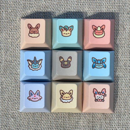 Nine pastel Pokémon Eeveelution keycaps featuring Eevee, Vaporeon, Jolteon, Flareon, Espeon, Umbreon, Leafeon, Glaceon and Sylveon.