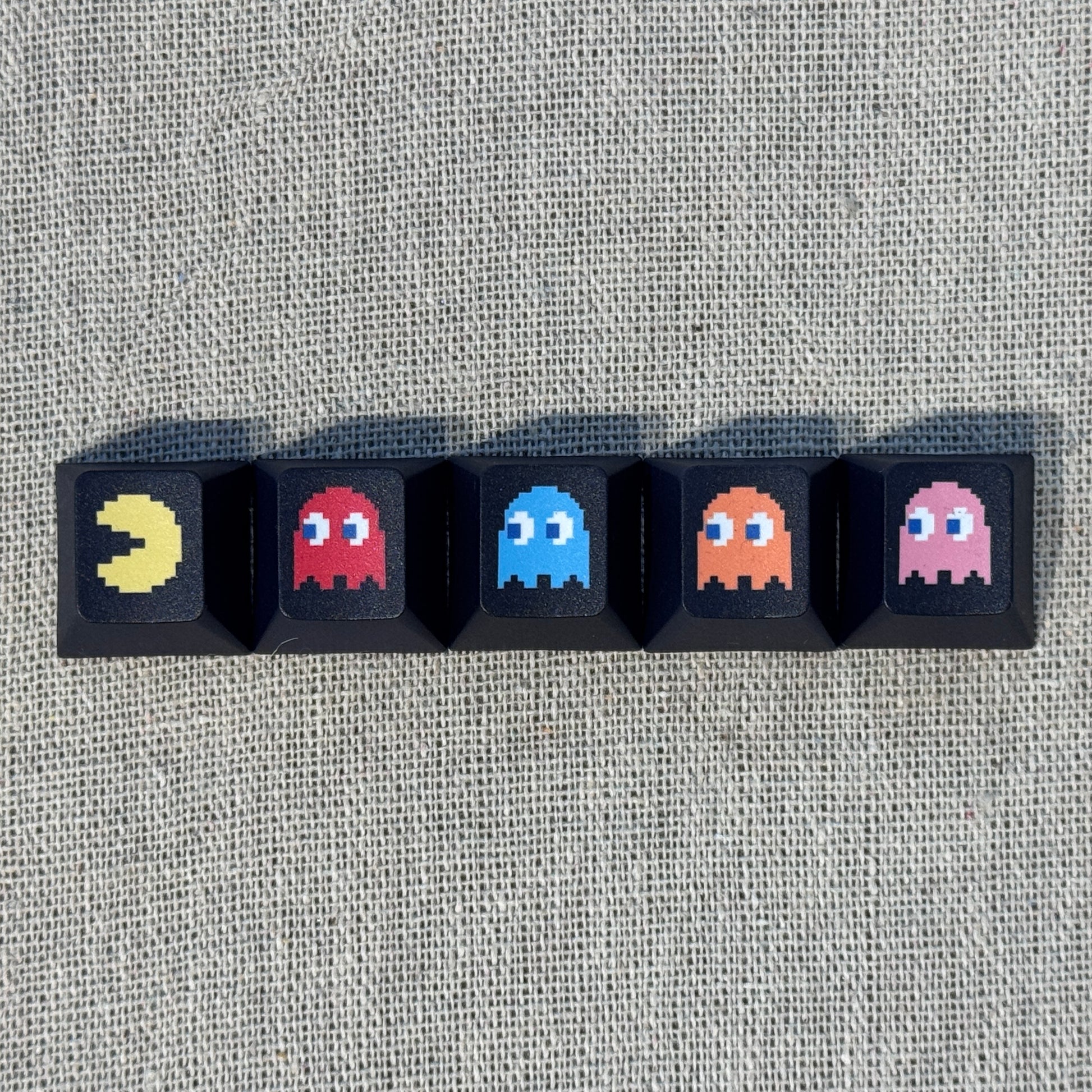 Five black Pac-Man keycaps featuring Pac-Man and the four ghosts Blinky, Inky, Clyde and Pinky arranged in a row.