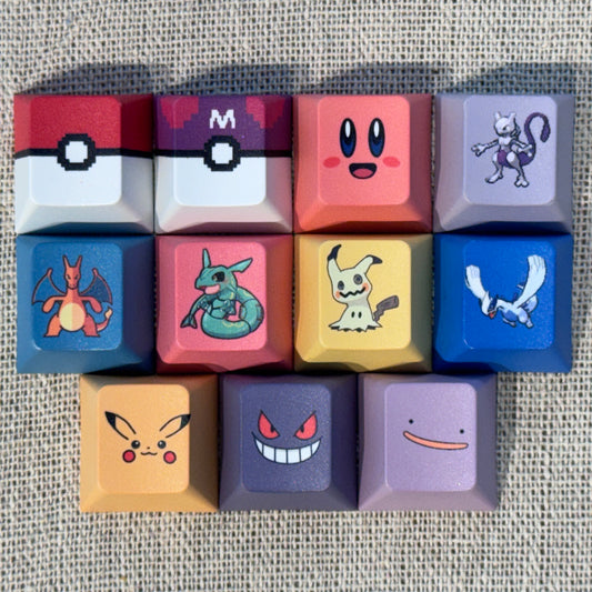 Eleven Pokémon and Kirby keycaps featuring Poké Ball, Master Ball, Kirby, Mewtwo, Charizard, Rayquaza, Mimikyu, Lugia, Pikachu, Gengar and Ditto.
